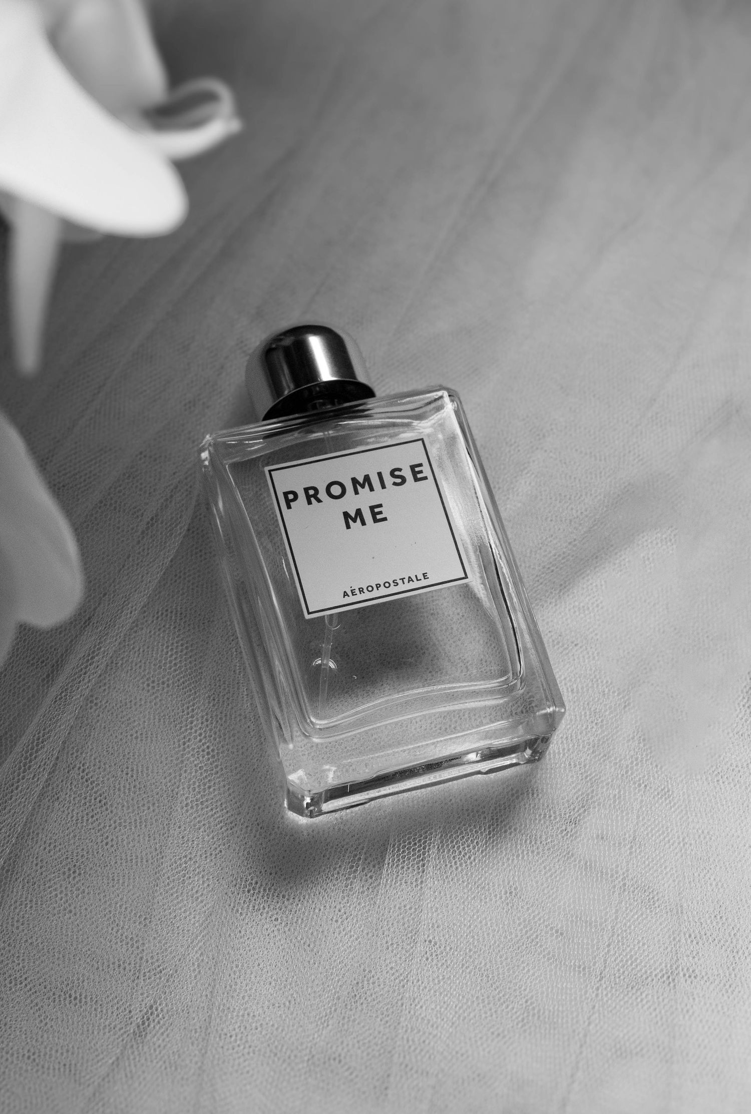 Black and white photo of 'Promise Me' perfume bottle on textured surface.