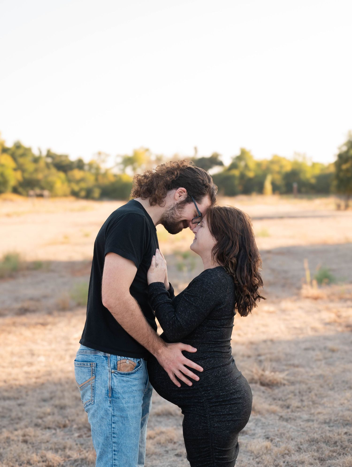 A couple embraces tenderly in an outdoor setting during golden hour.