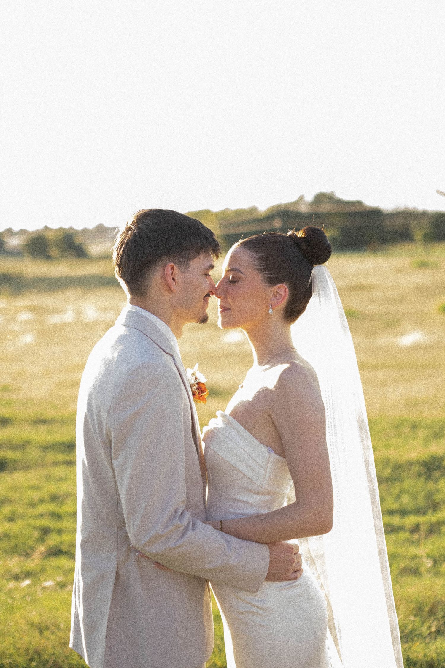 Romantic sunset portrait of newlyweds embracing in golden field.
