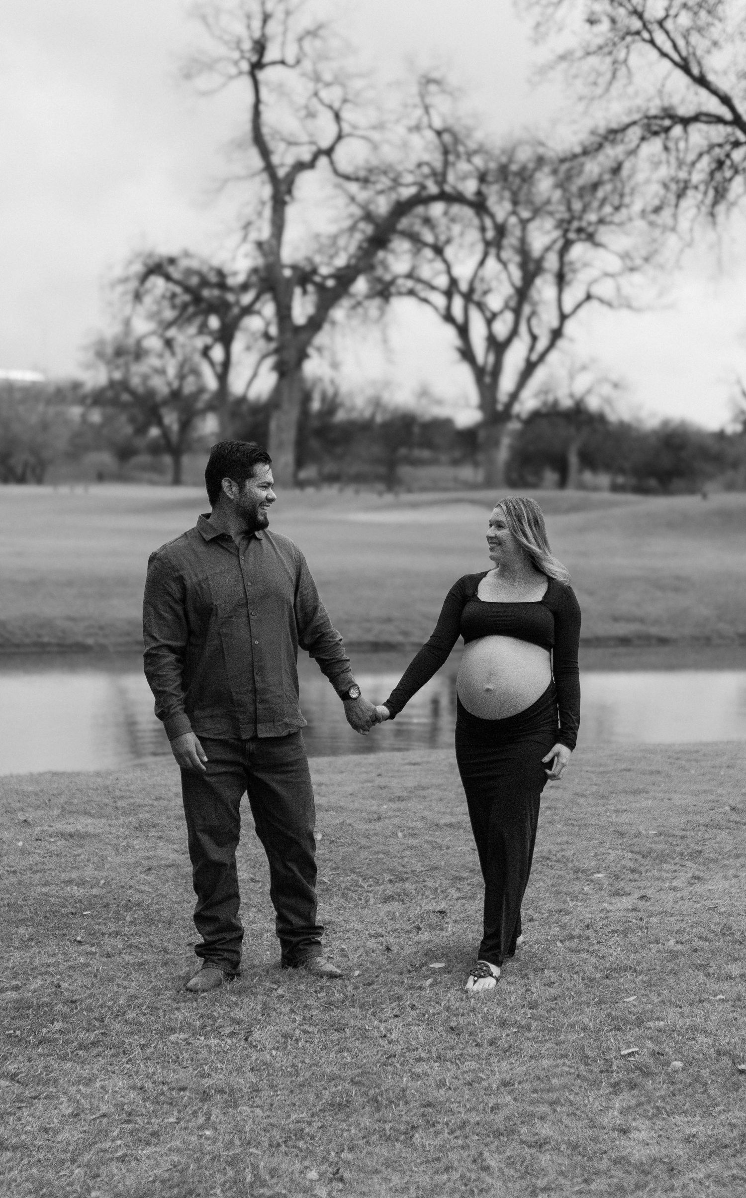 A couple poses for a series of black and white maternity photos in an outdoor field with bare trees.