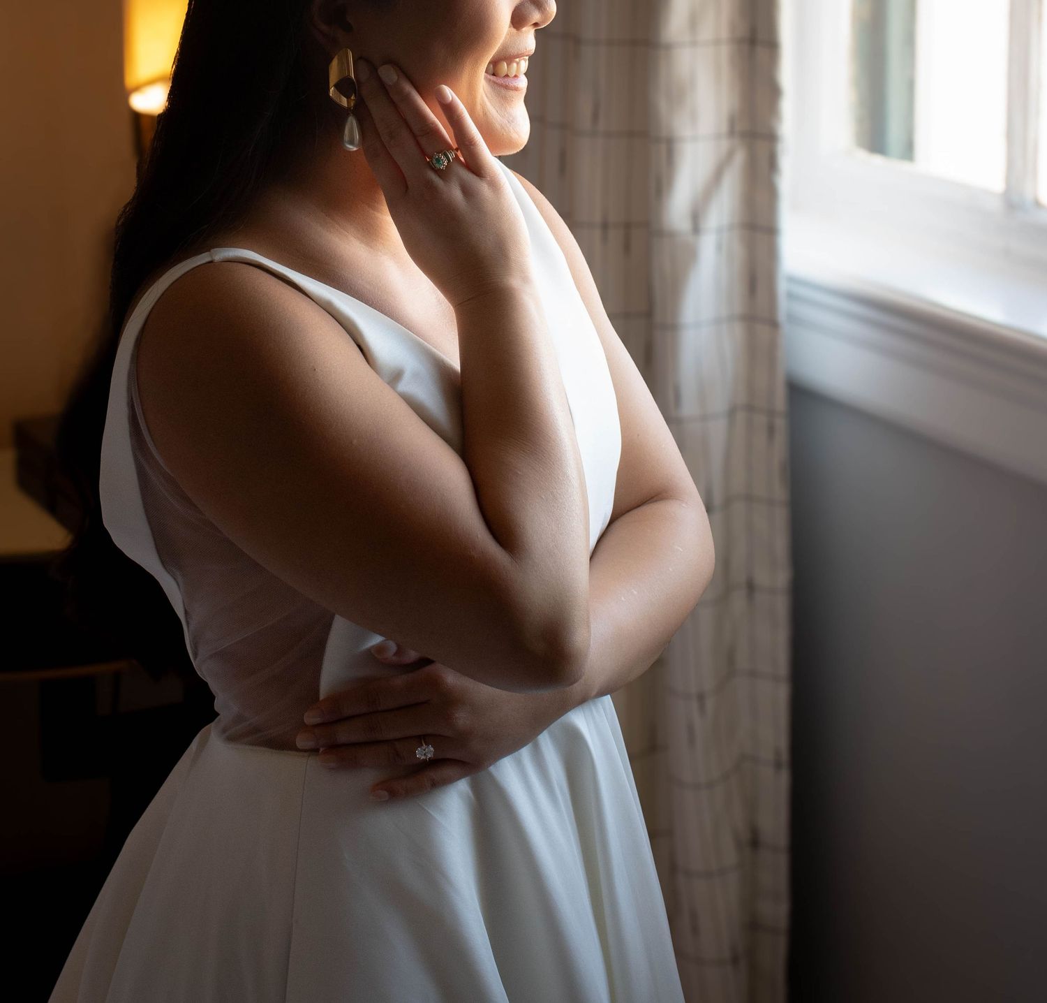 Soft window light illuminates a bride in her wedding dress creating an intimate moment.