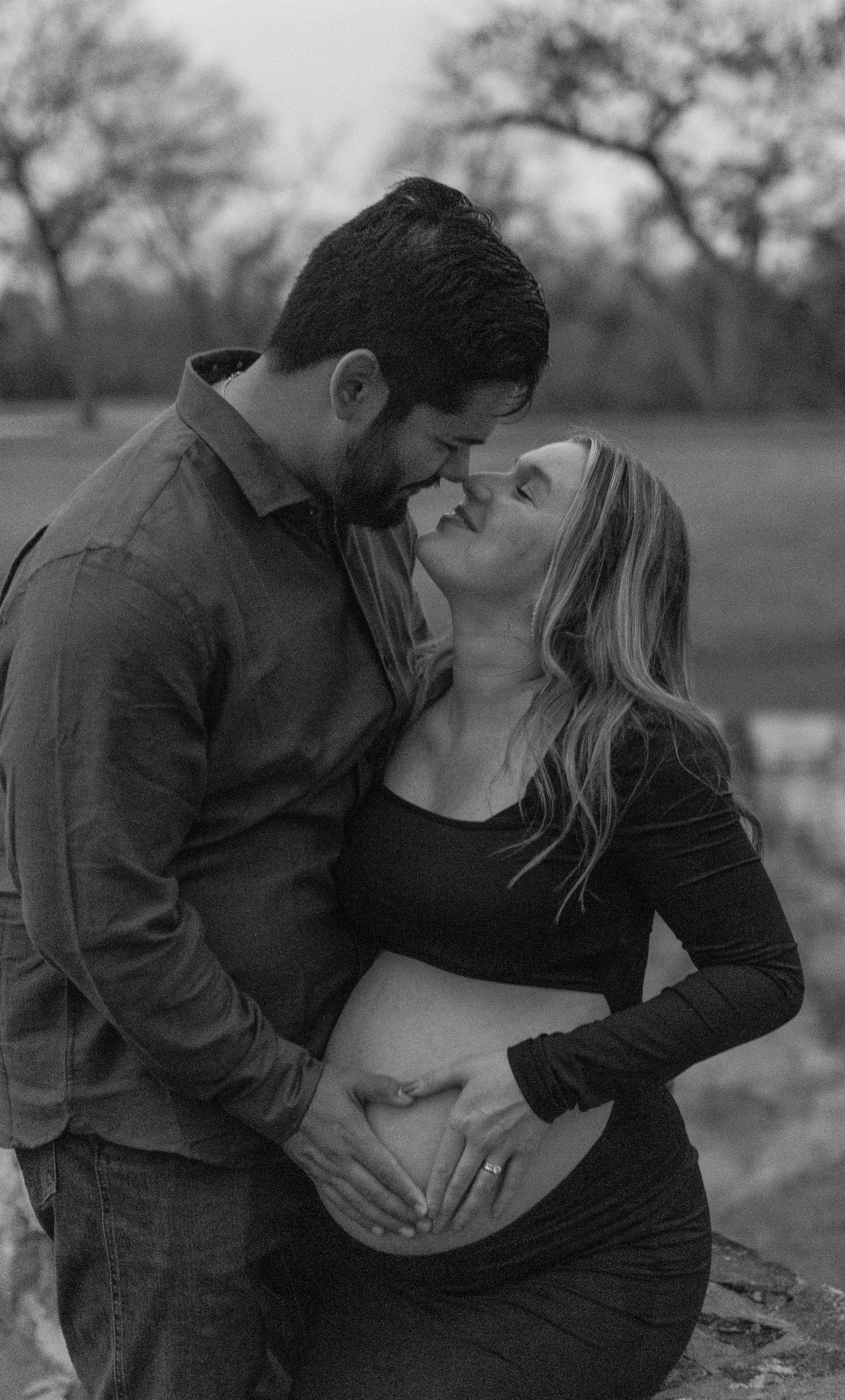 Intimate black and white maternity photoshoot showing couple embracing outdoors.