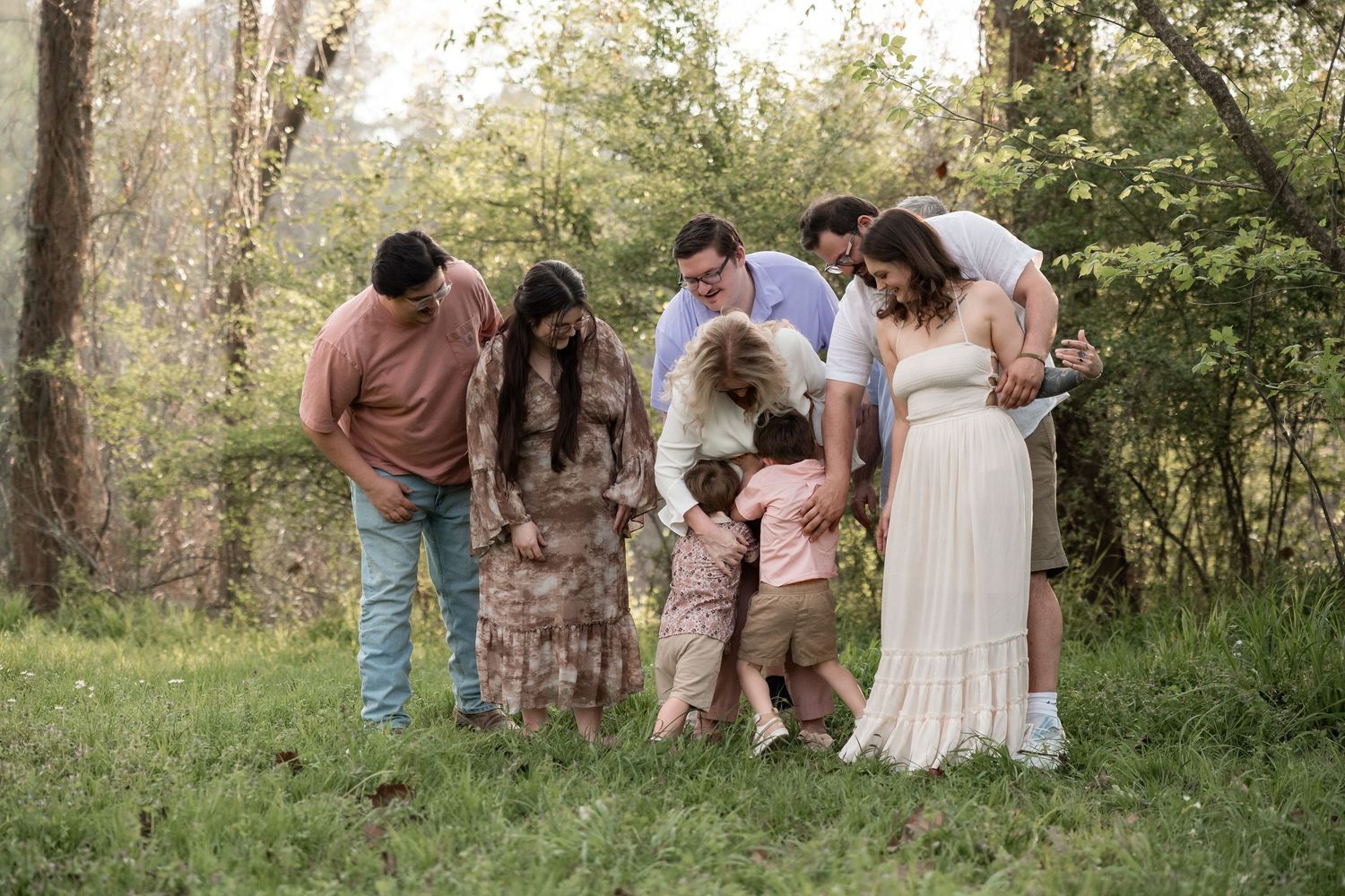 Family gathering outdoors in a lush green setting, with a pregnant woman in a white dress surrounded by loved ones.