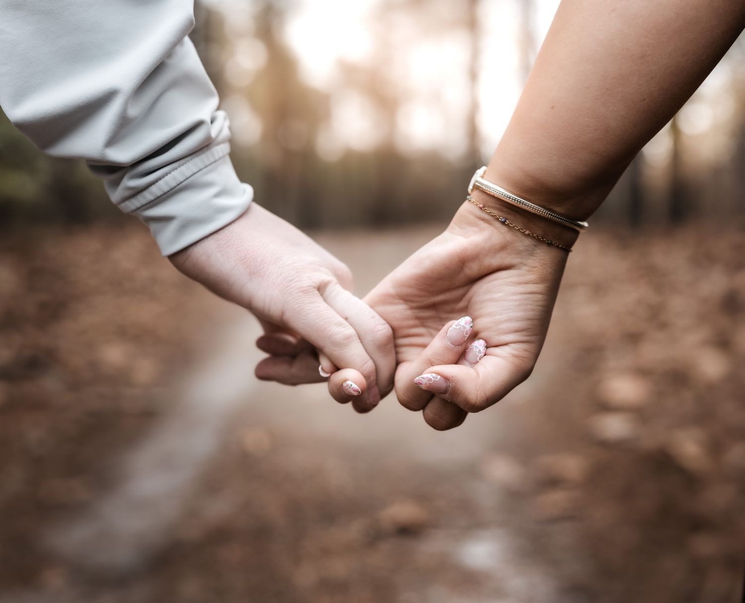 Two hands tenderly holding each other in a romantic gesture against a blurred outdoor forest background.