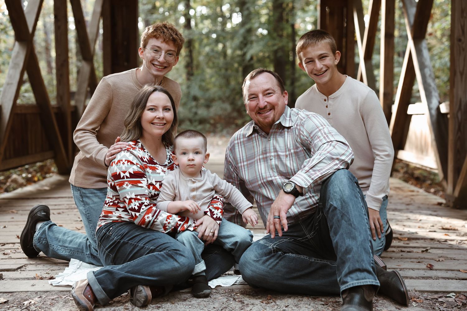 Family sits together on wooden boardwalk in casual clothing for outdoor portrait.