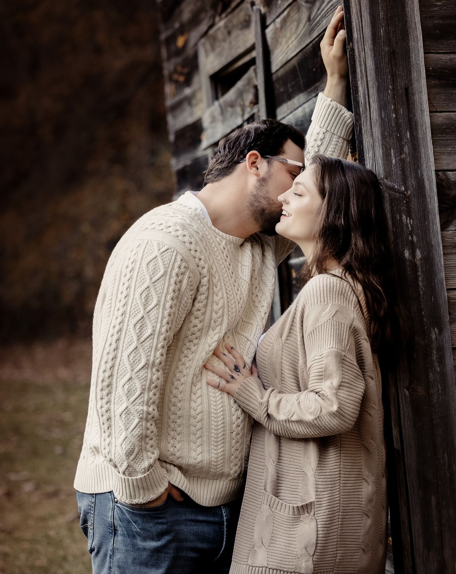 Couple wearing matching cream cable knit sweaters share intimate moments in a rustic outdoor setting.