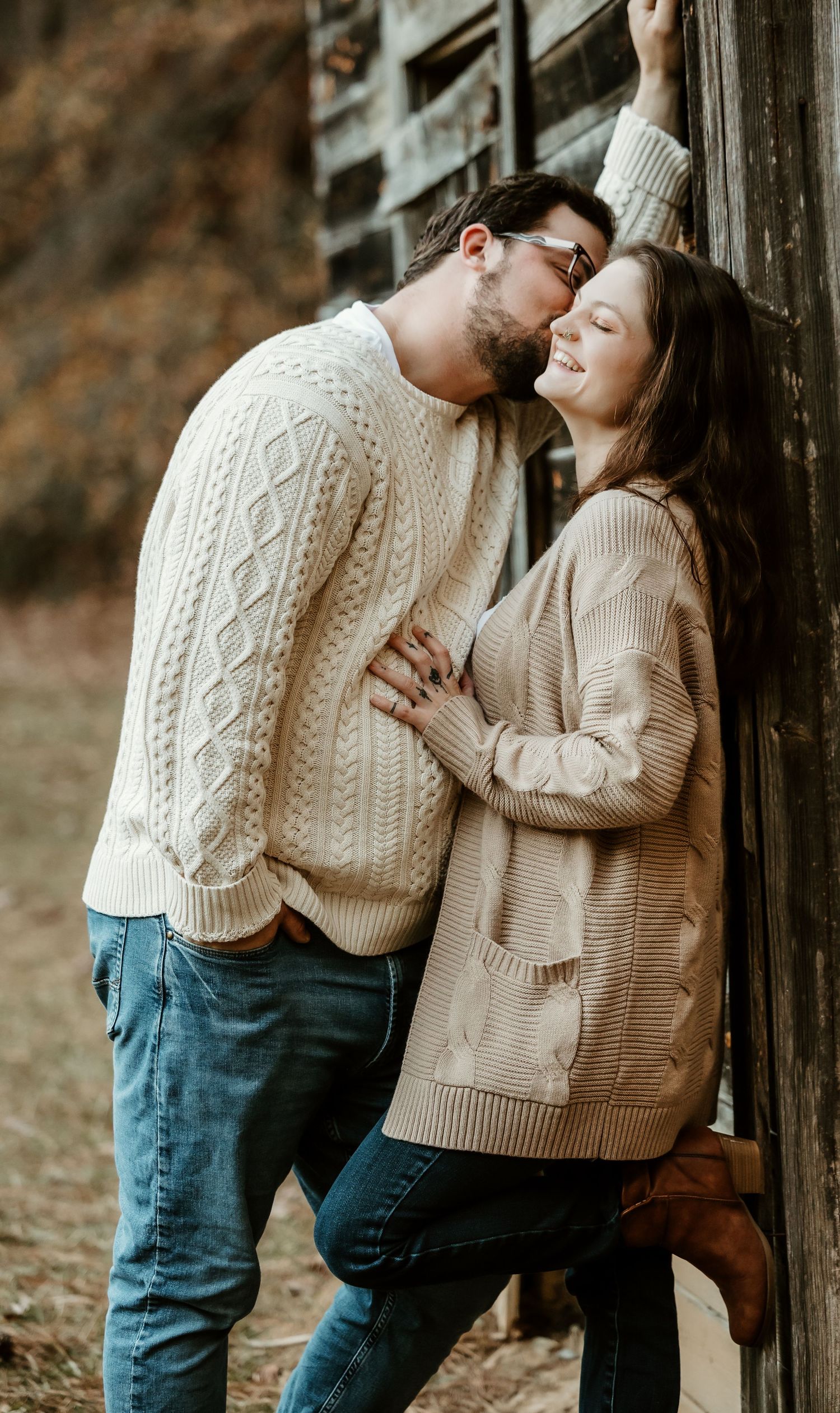 Romantic couple in matching knit sweaters embracing outdoors against wooden posts.