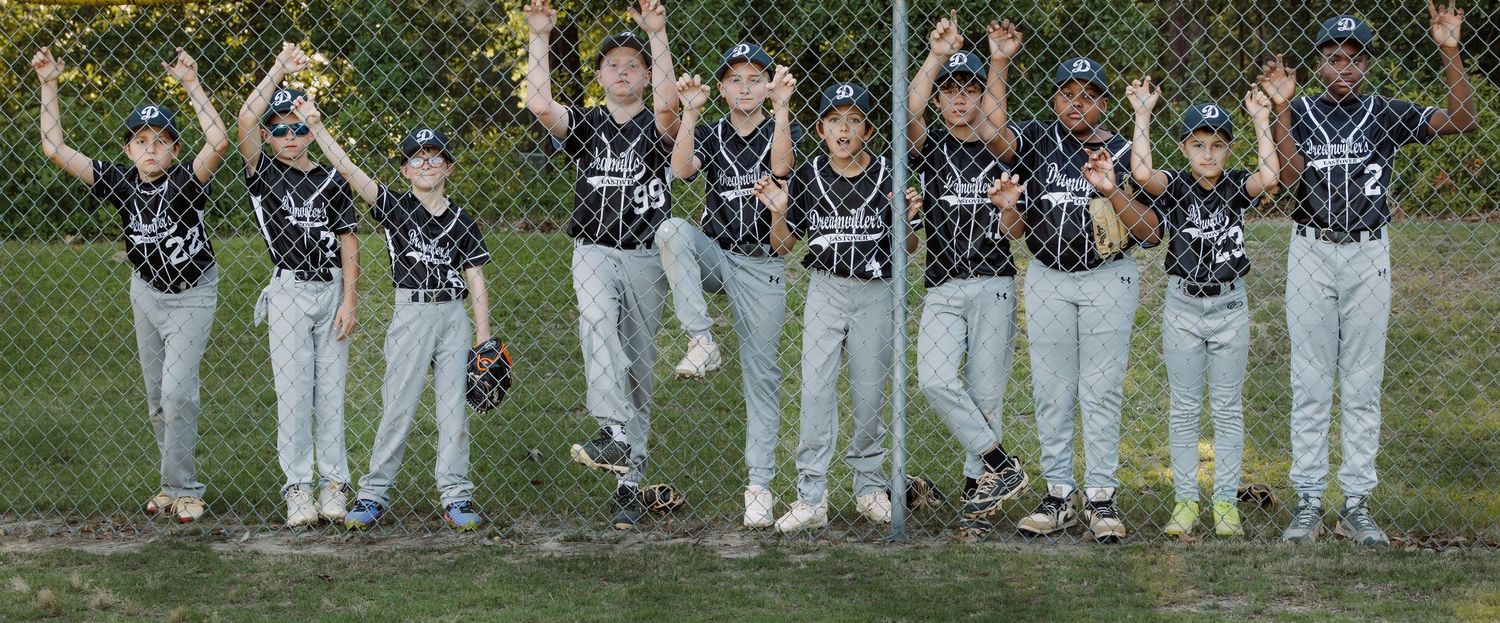 Youth baseball team celebrating with raised arms on field in dark uniforms.