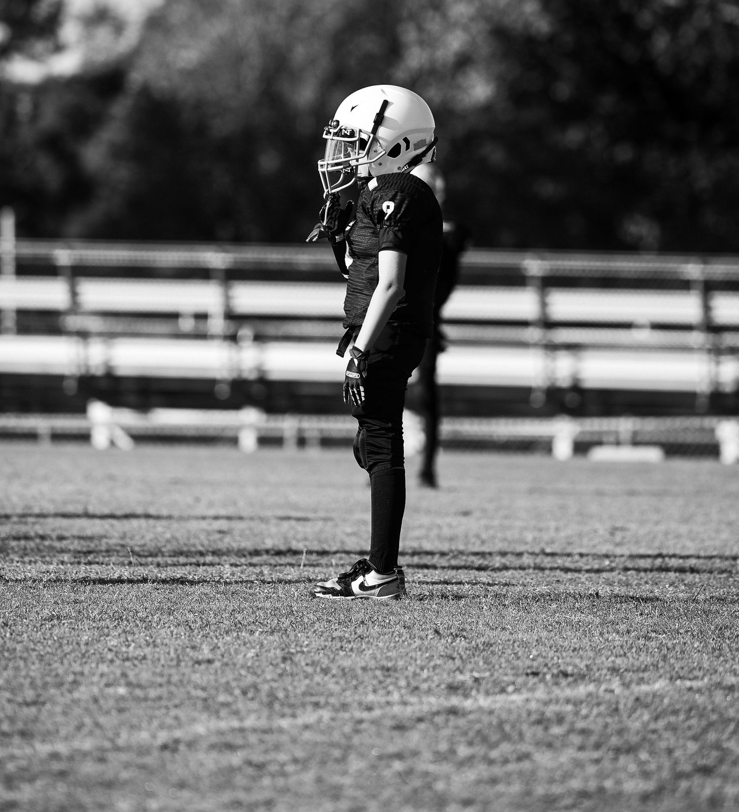A black and white image shows a football player's cleats on a grass field during a game.