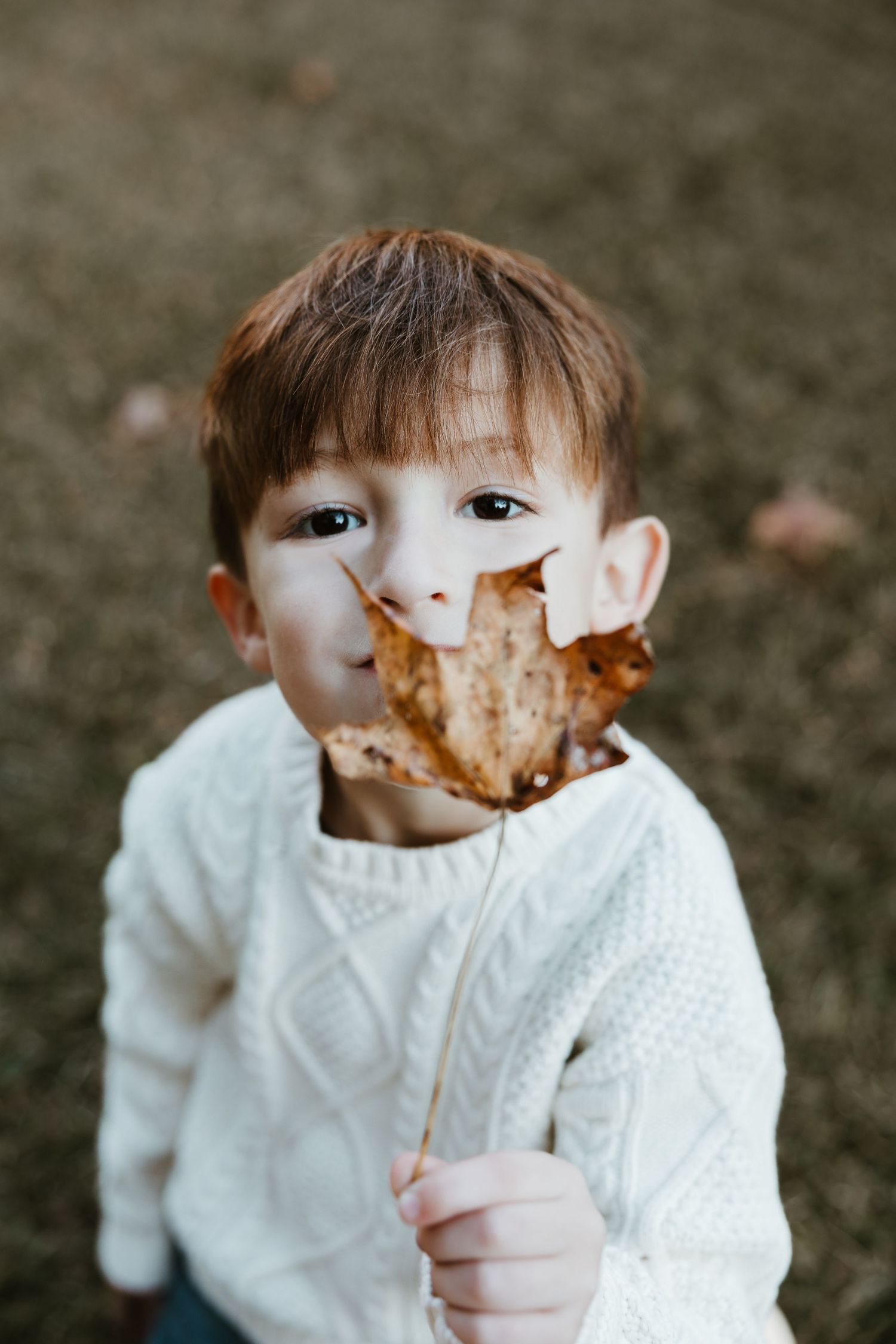 Child in white sweater enjoys a messy chocolate dessert outdoors.