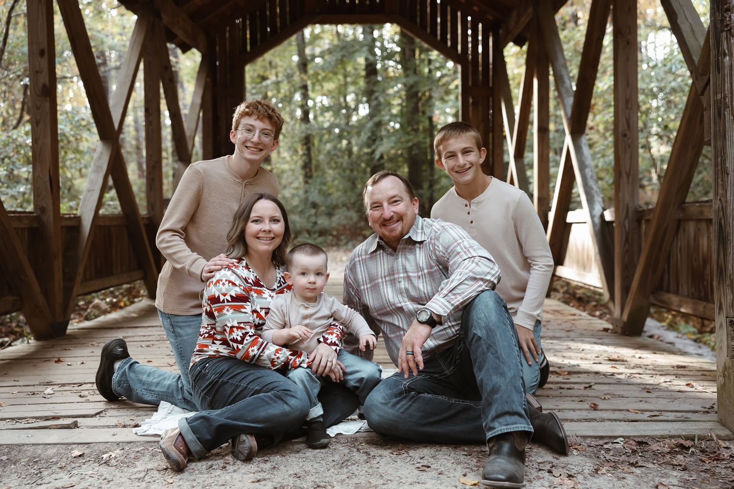 Family portrait session on rustic wooden bridge in forest setting.