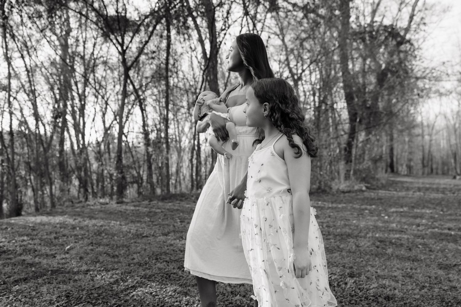 Black and white photo of two girls in white dresses playing outdoors among bare trees in a grassy field.