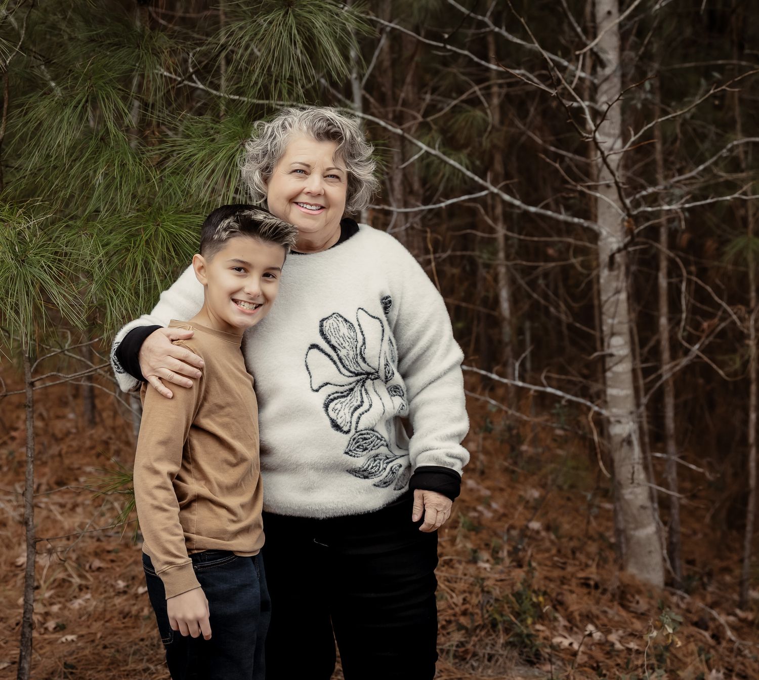 A couple in casual winter attire embraces and laughs together during an outdoor photo session in a wooded setting.
