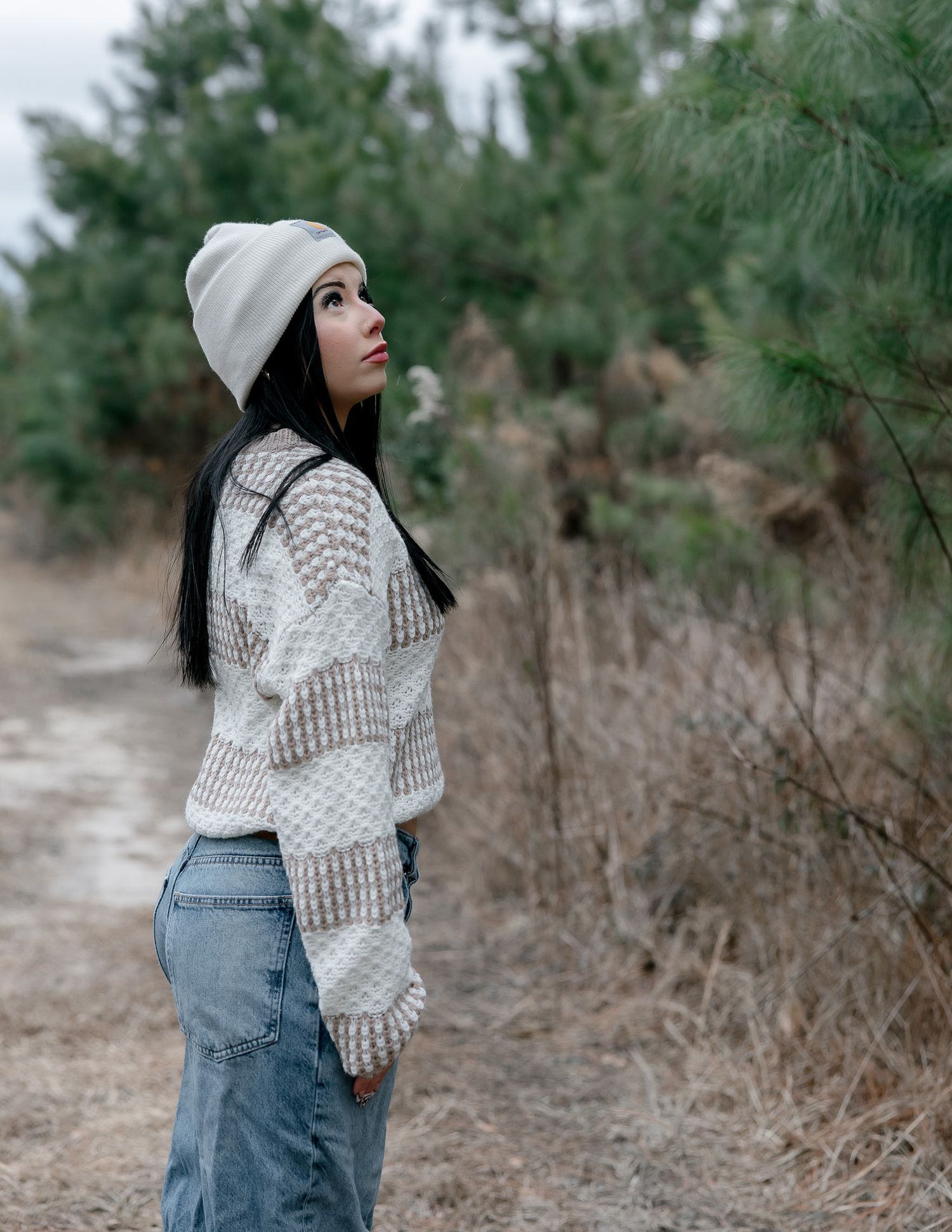 Winter portrait series in pine forest with person wearing white knit sweater and beanie.
