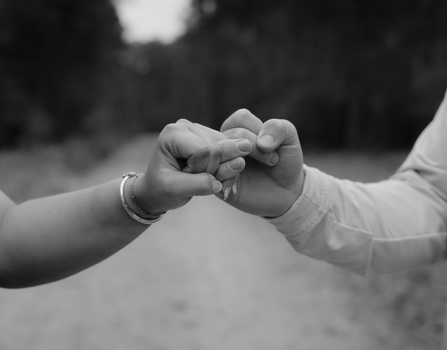 Black and white photo of two people interlocking fingers outdoors, symbolizing connection and togetherness.