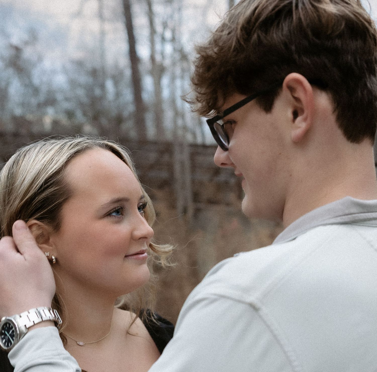 A young couple shares a romantic moment outdoors, with the man gently touching the woman's hair.