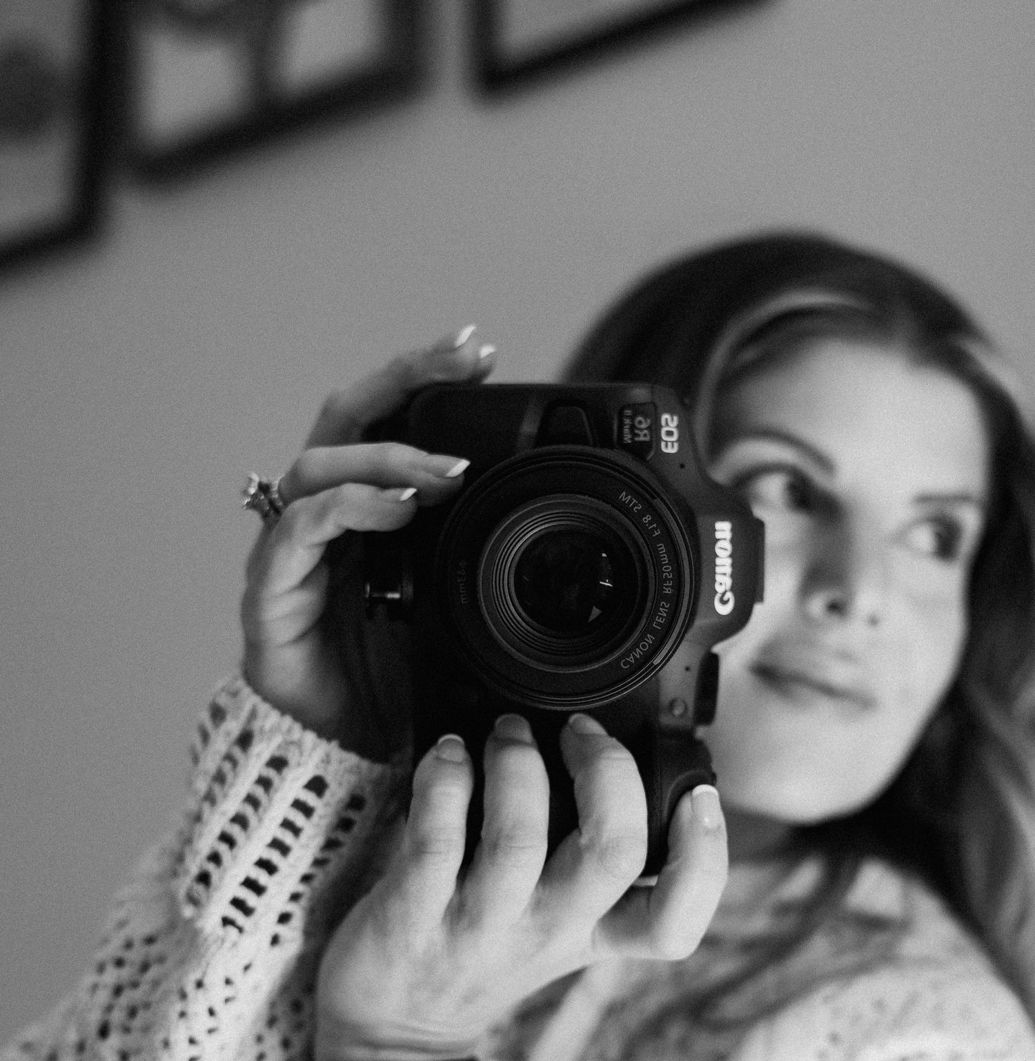 A photographer in a white knit sweater holds a camera in black and white tones.