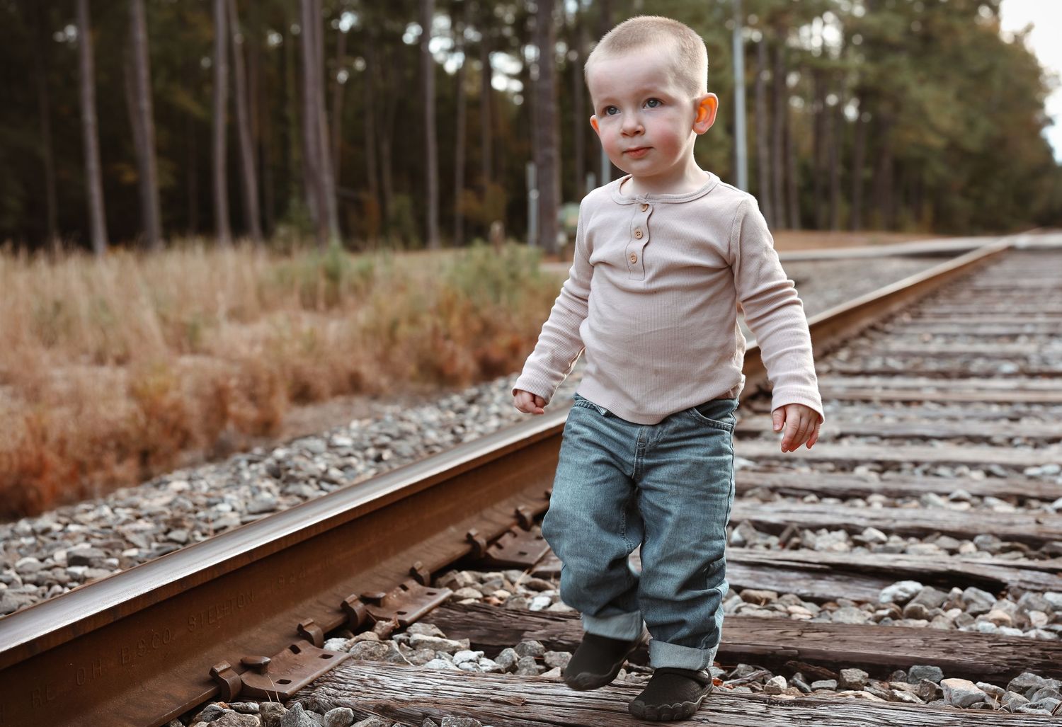 Child walks along train tracks in casual clothing on a sunny day.