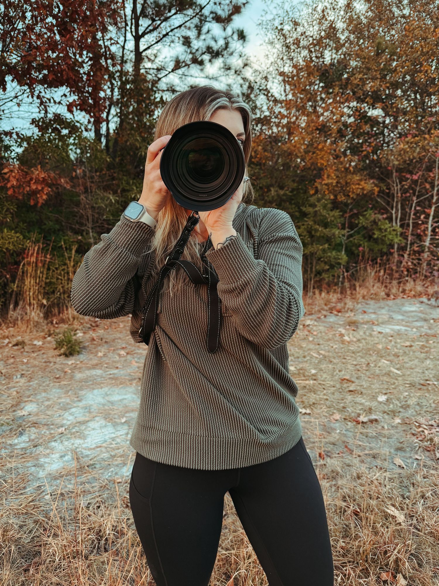 Photographer in gray sweater taking photos in autumn forest setting.