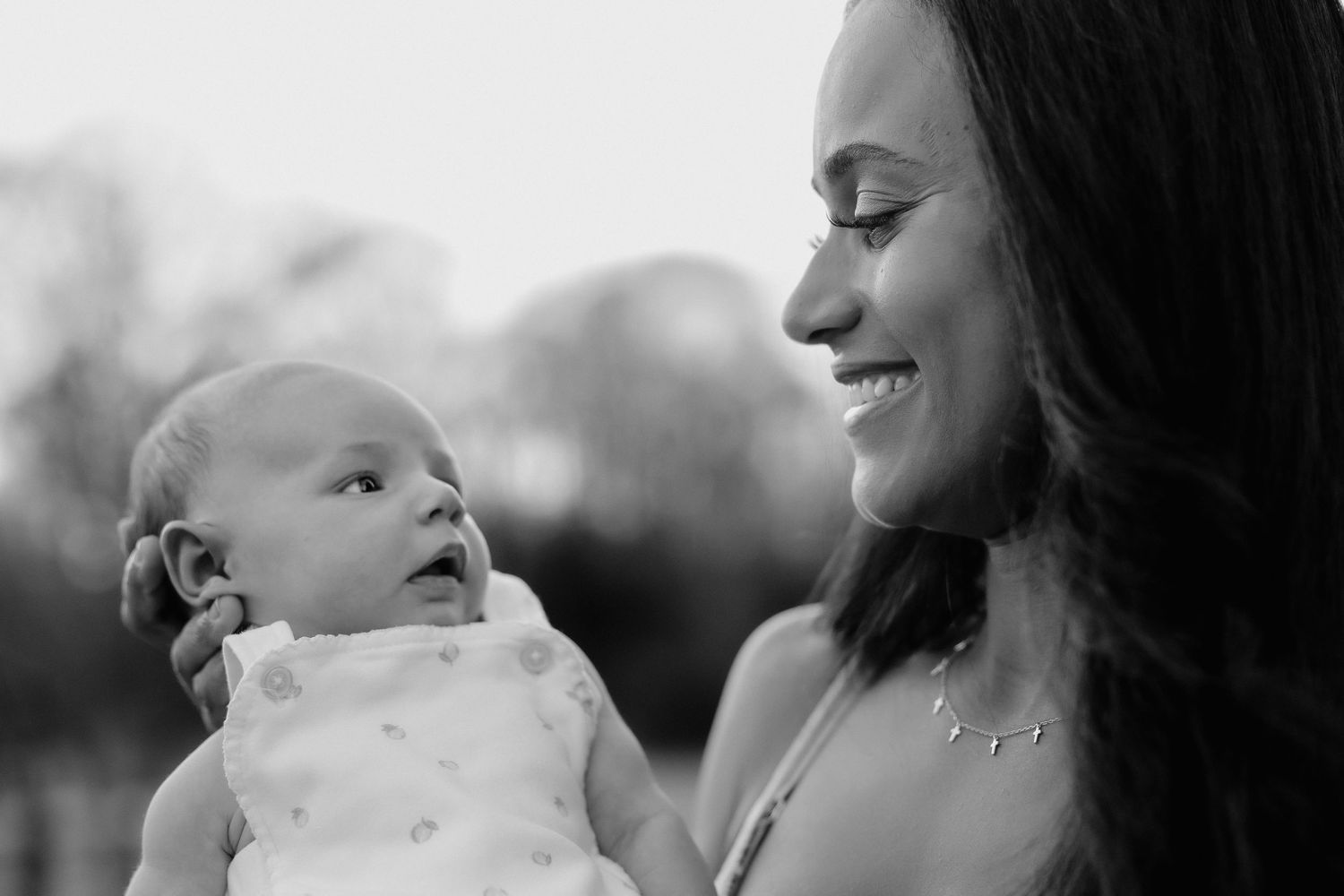 Black and white photo of a smiling woman holding a newborn baby outdoors.