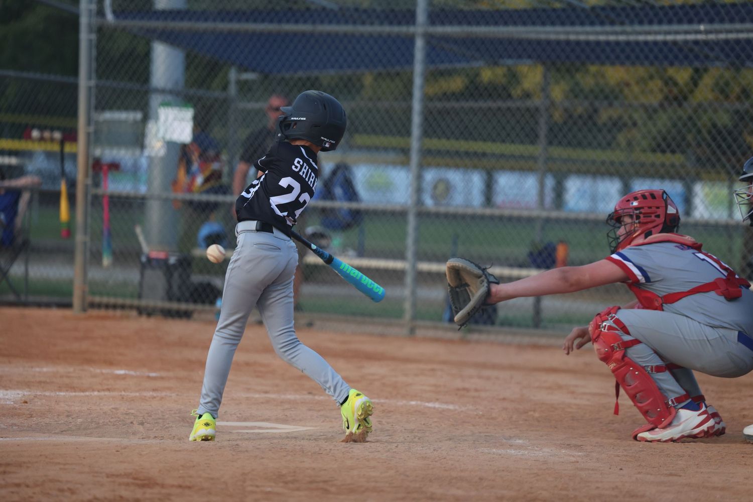 Young baseball player in black uniform swings bat during youth league game as catcher waits behind home plate.