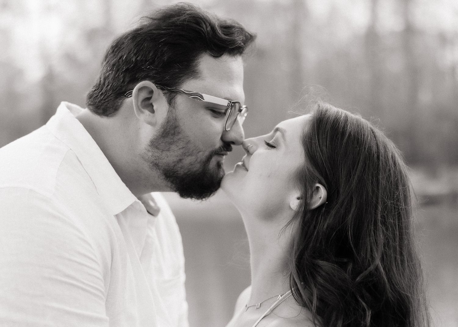 Couple sharing a romantic kiss in a black and white outdoor engagement portrait.