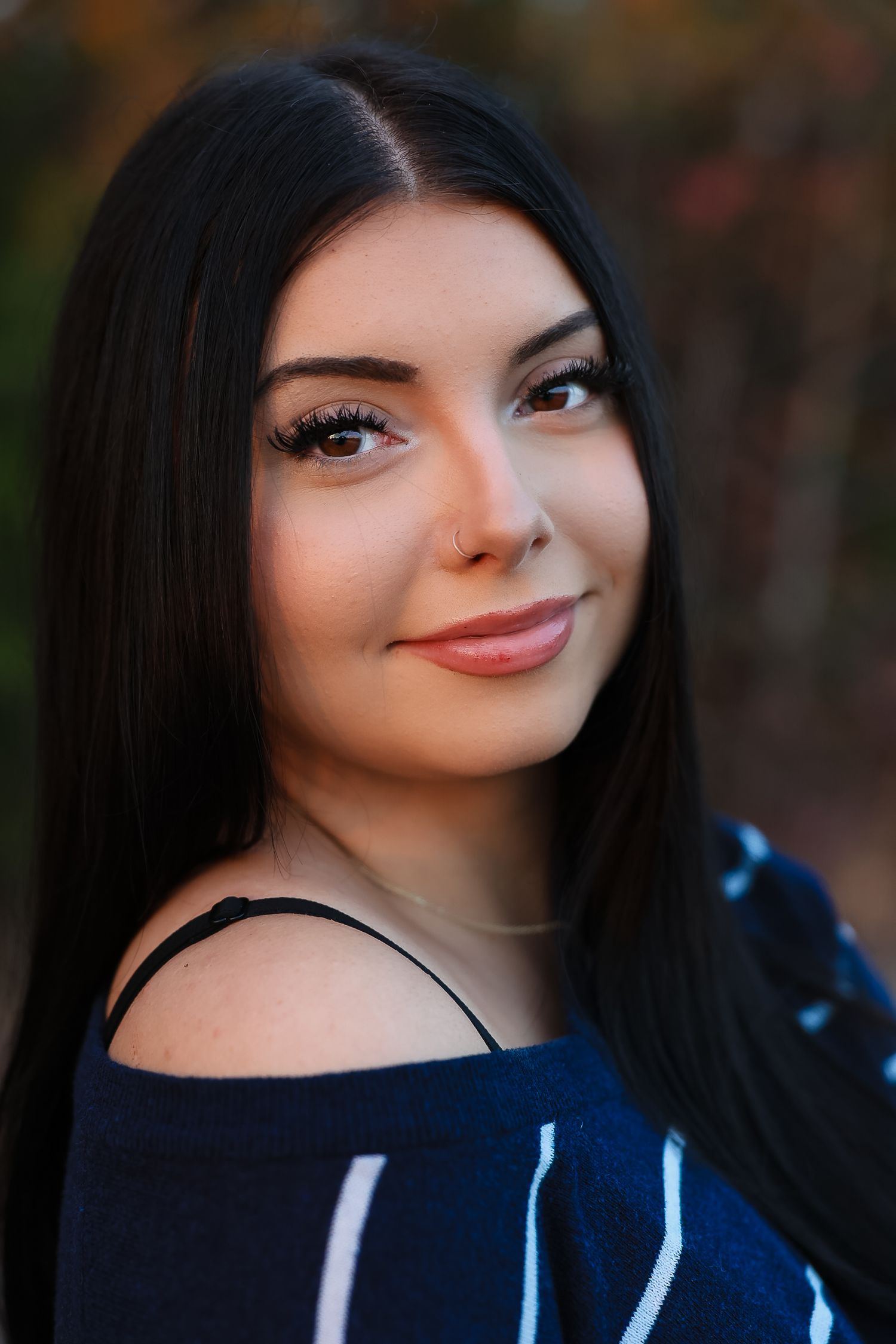 Portrait of woman with long dark hair wearing black top against natural background.