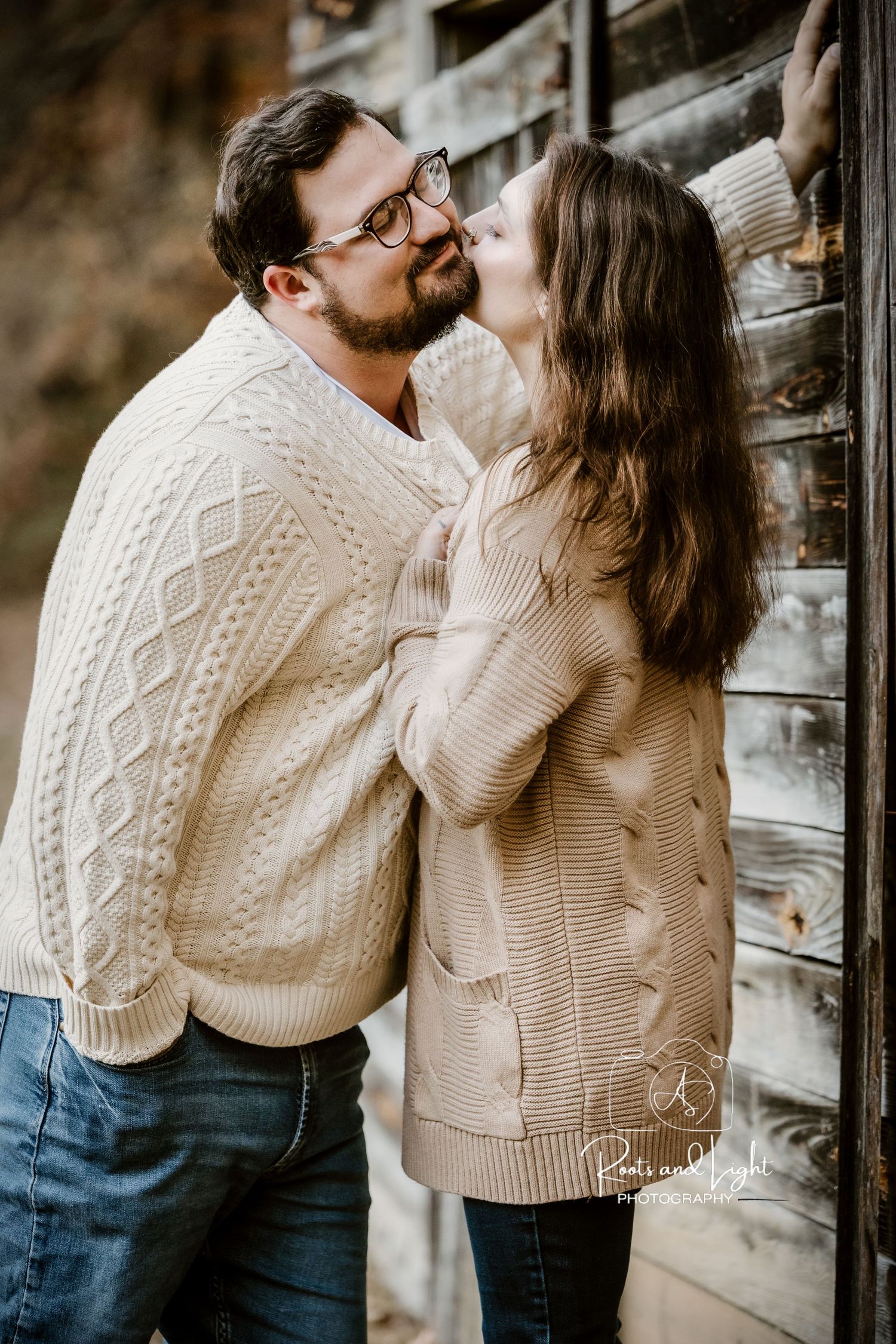 Romantic couple in cable knit sweaters embracing against rustic backdrop.