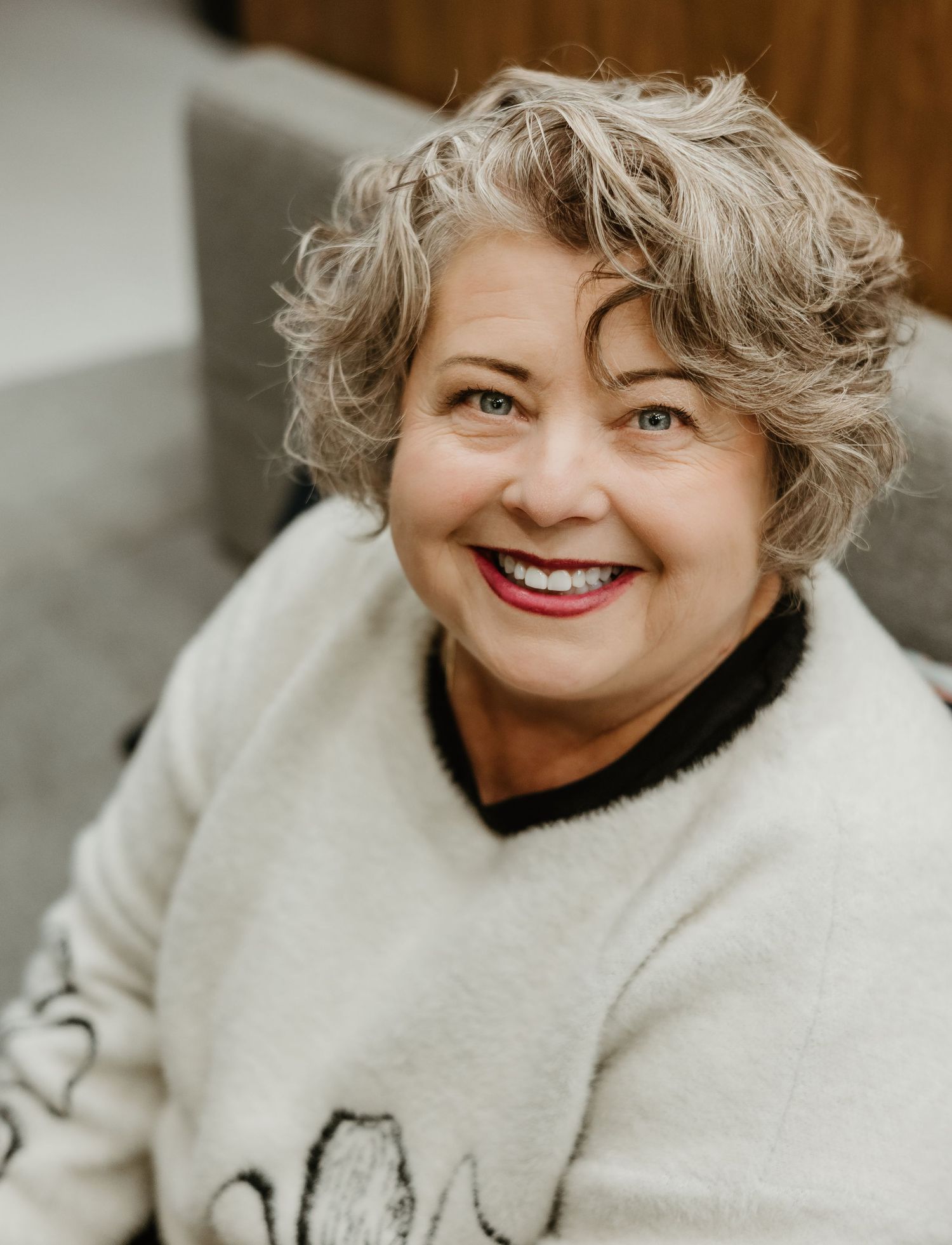 A person in a cream colored sweater smiles warmly while looking off to the side.