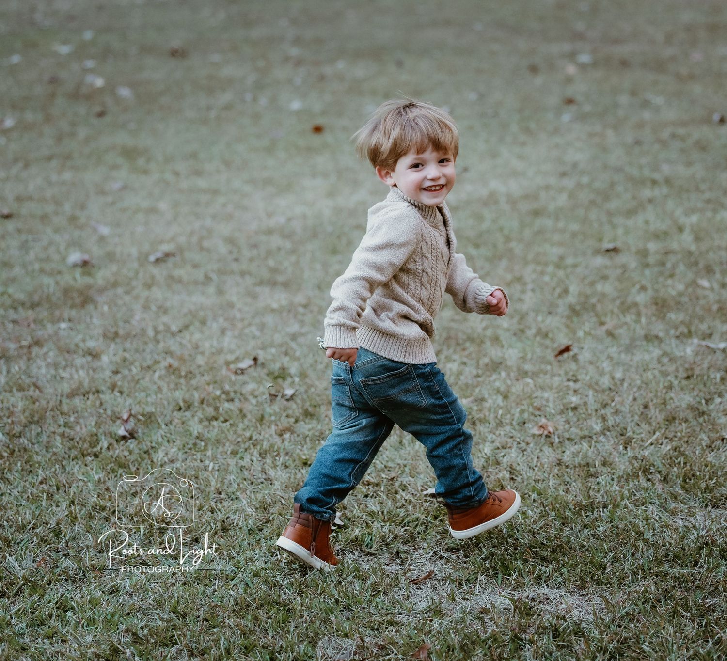 Sequence of a toddler running and playing on grassy ground wearing brown sweater and jeans.