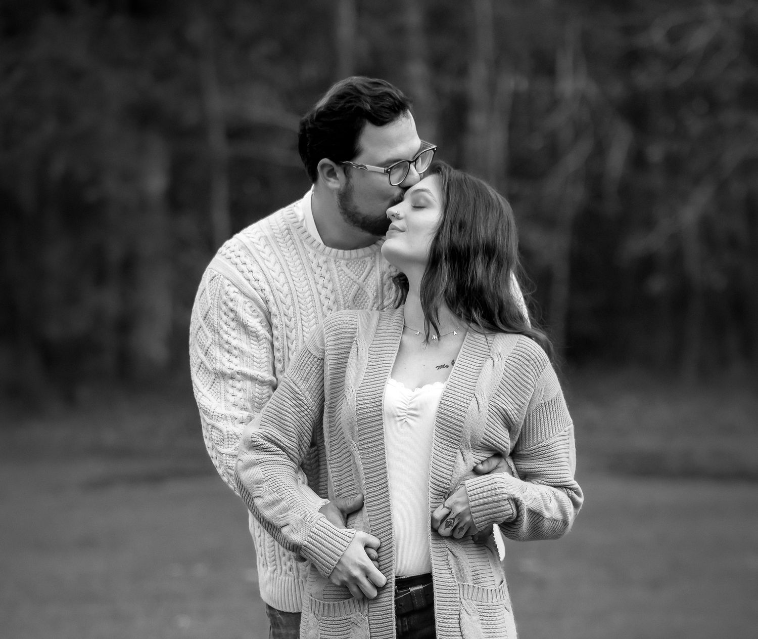 A couple in matching white sweaters embrace lovingly in a romantic outdoor photoshoot.
