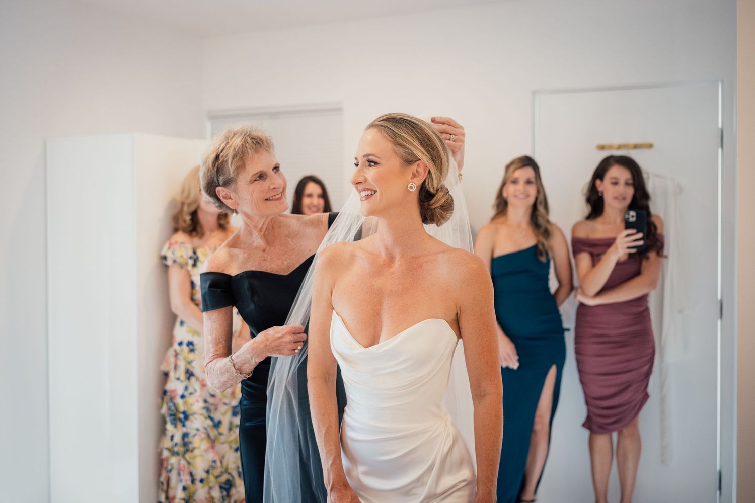 Louis Willard Photo Palm Springs Bride in white strapless gown smiles as bridesmaids help adjust her veil before the wedding ceremony.