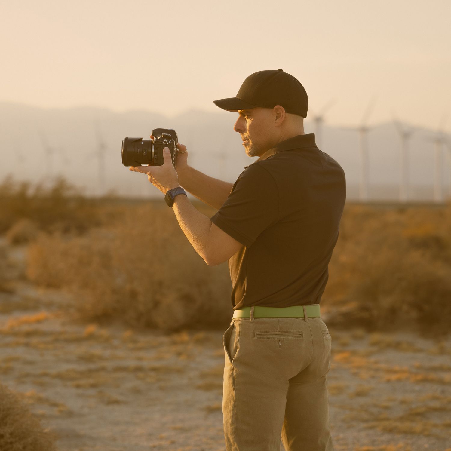 Photographer capturing desert landscape at golden hour with wind turbines in background.
