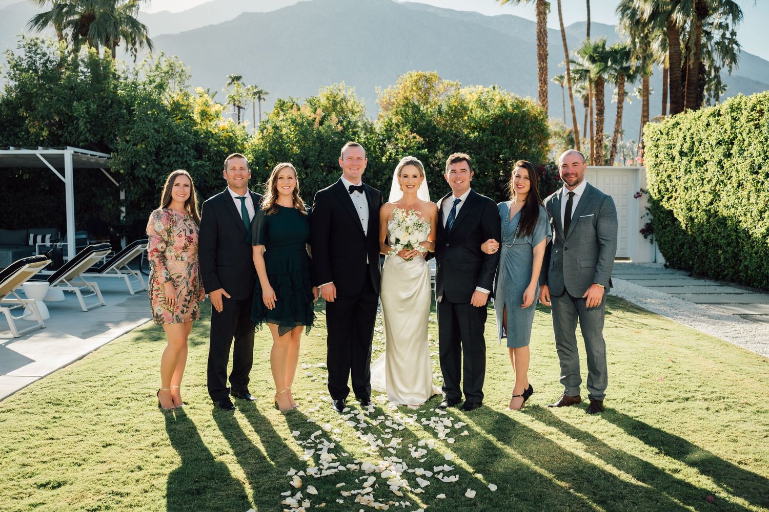 Louis Willard Photo Palm Springs Wedding party poses together on a sunny lawn with mountain views at a Palm Springs wedding.