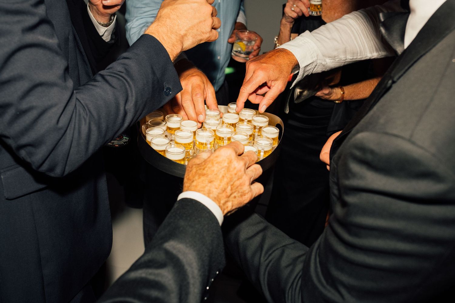 Louis Willard Photo Palm Springs Wedding guests reach for shot glasses on a tray during a lively cocktail hour celebration.