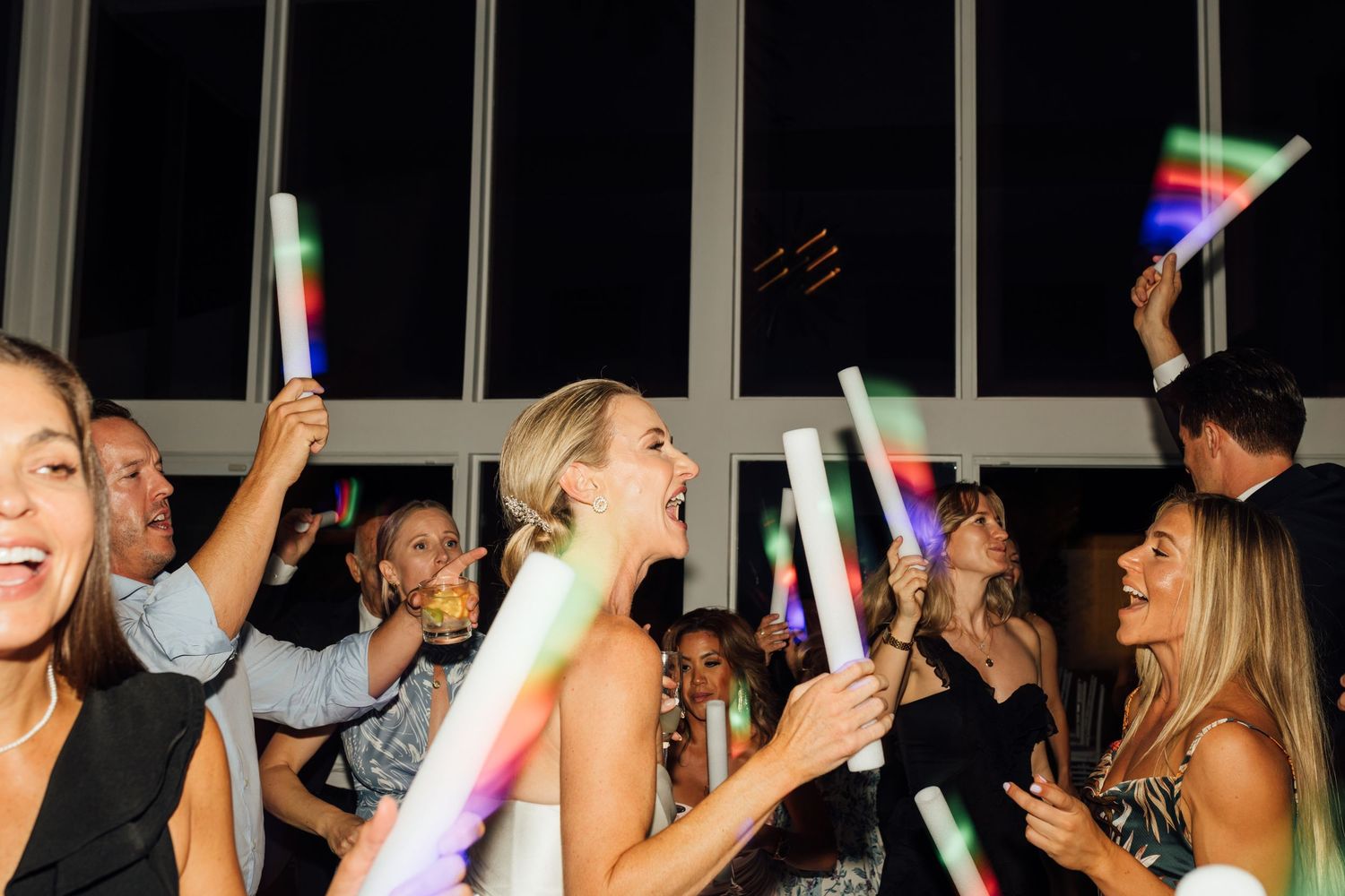 Louis Willard Photo Palm Springs Bride and guests wave colorful LED foam sticks on the dance floor during a lively wedding reception.