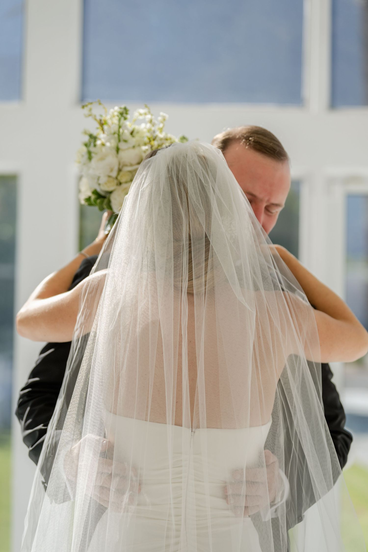 Louis Willard Photo Palm Springs Groom embraces bride from behind during an emotional first look, her veil cascading down her back.