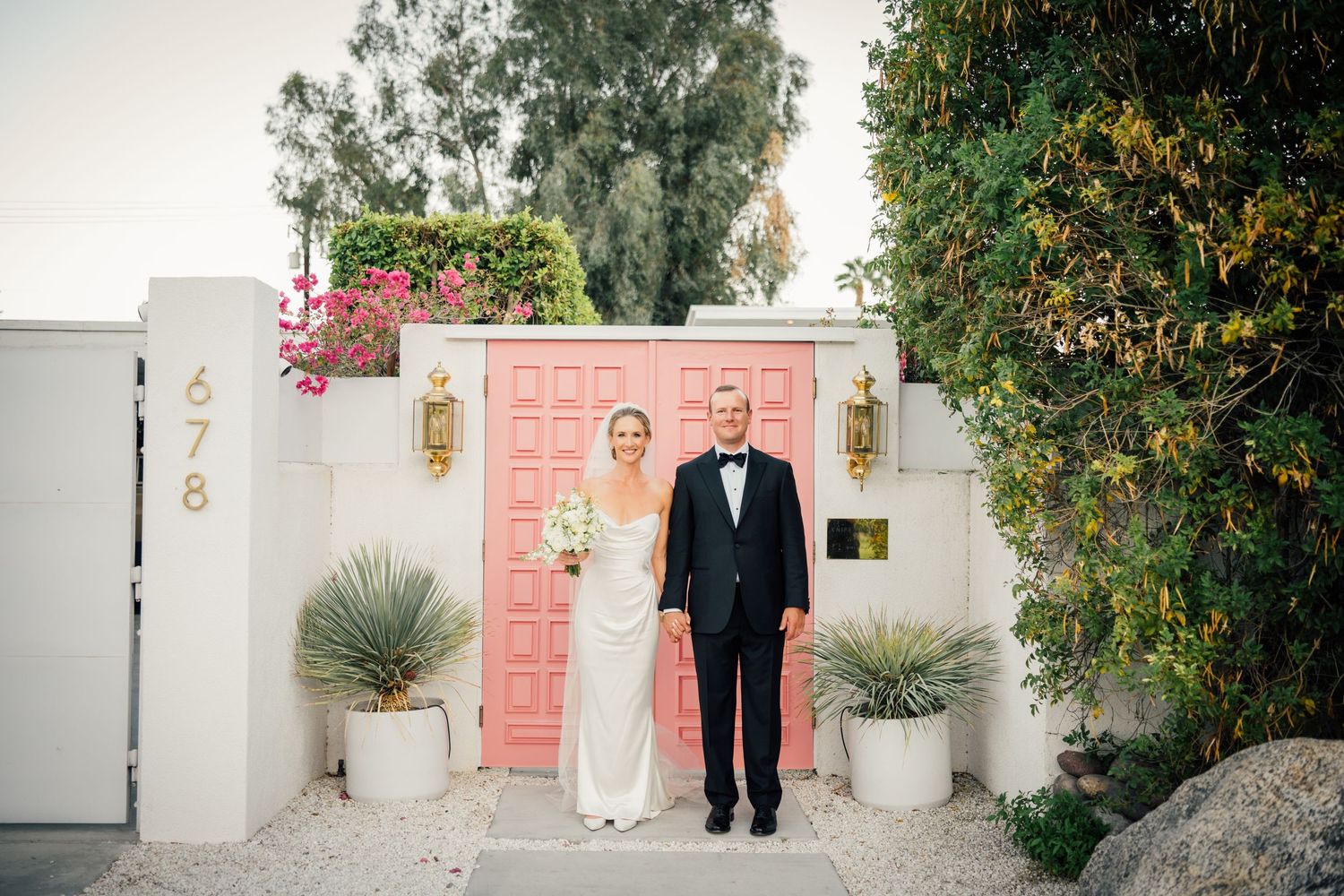Louis Willard Photo Palm Springs Bride and groom pose together in front of iconic pink doors at Palm Springs venue.