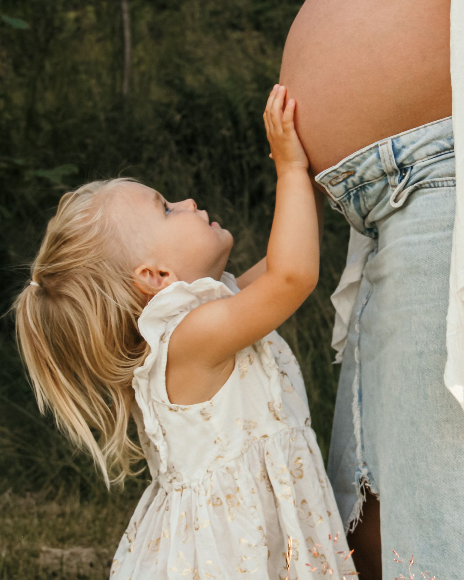Graviditetsfotografering - en liten flicka som håller sin mammas mage utomhus i Jönköping