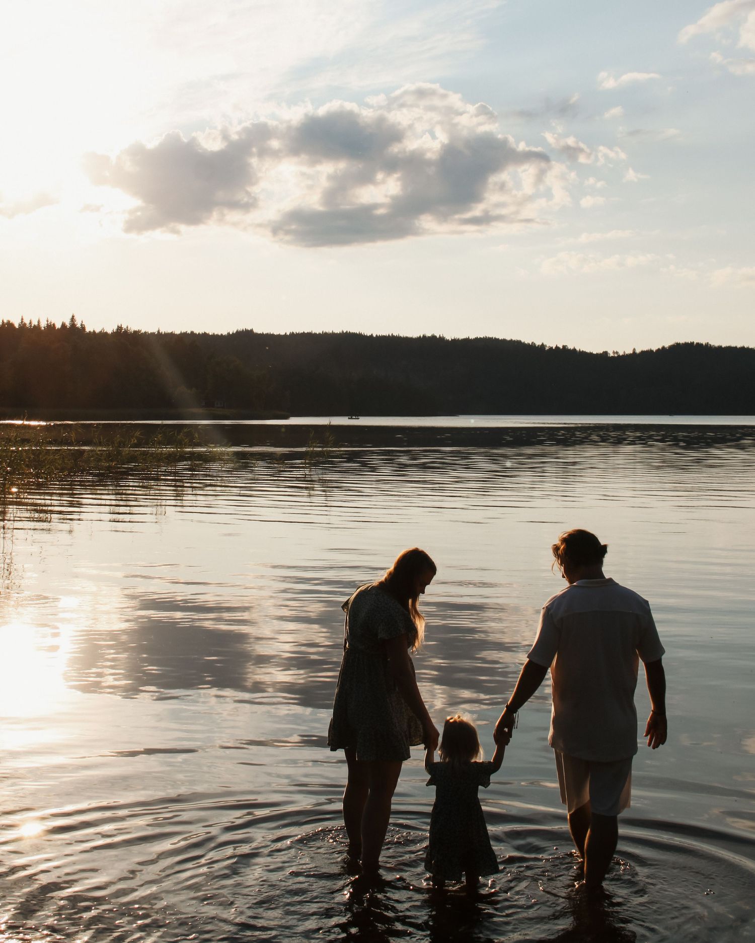 Familjefotografering - två föräldrar med sitt barn i en sjö i Jönköping i mjukt kvällsljus