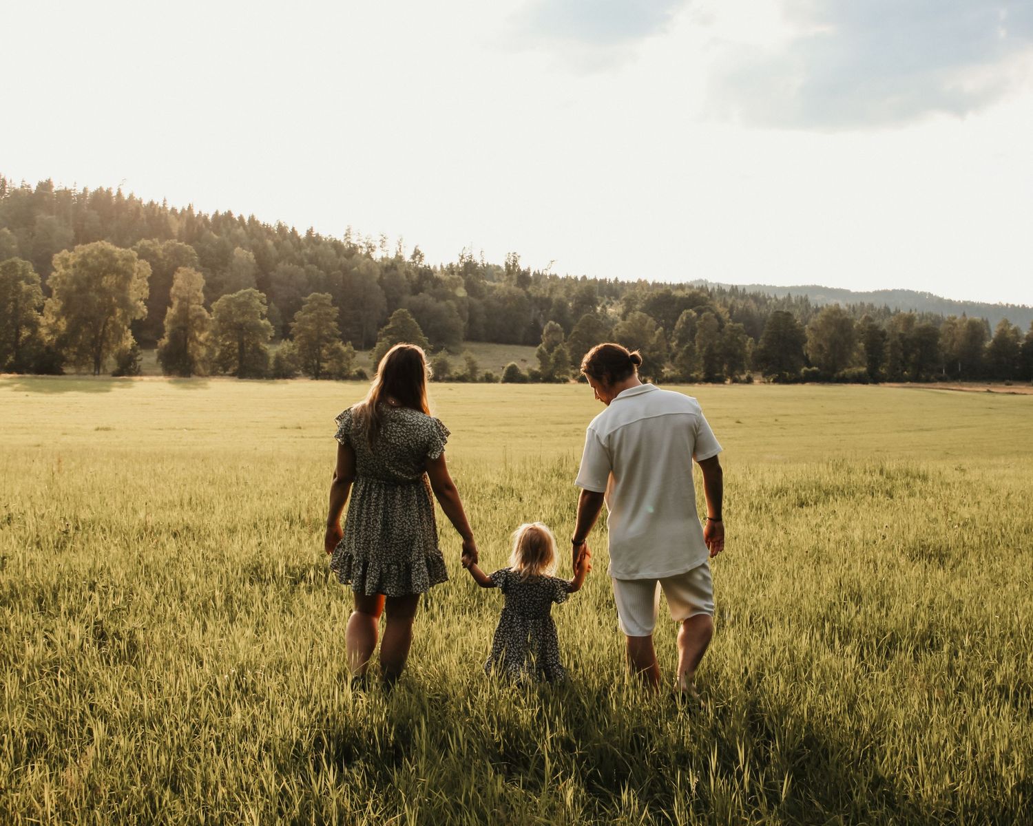 Familjefotografi - En familj med ett litet barn som går i ett fält i Jönköping i mjukt sommarkvällsljus