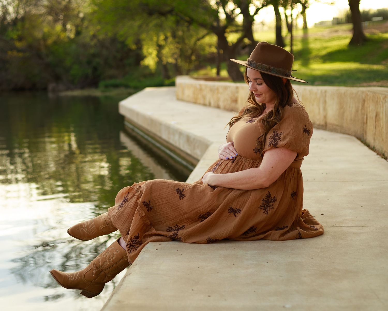 Person in brown dress relaxing by tranquil water's edge on sunny afternoon.