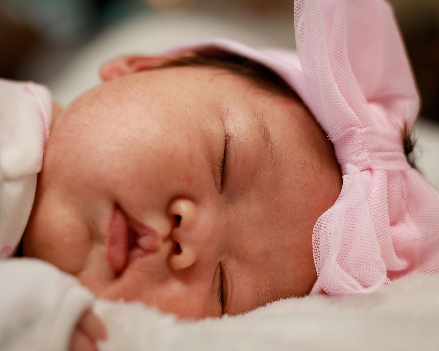 Peaceful newborn baby sleeping in a pink hat and outfit, with soft delicate features and rosy skin.