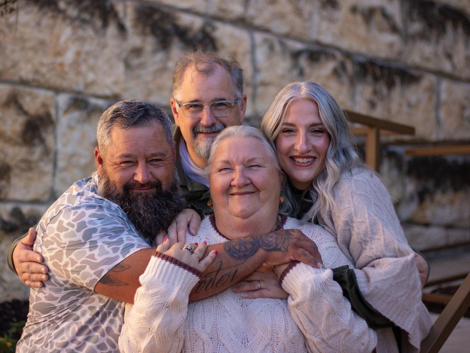 A group of people embrace and smile together in a casual outdoor family photo session.