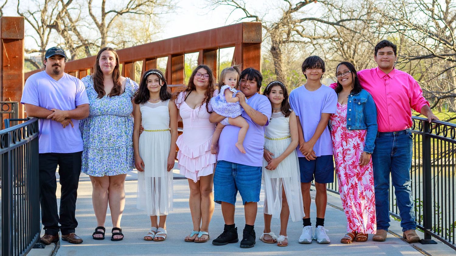 Large family group portrait on a bridge outdoors, smiling together in spring casual attire.