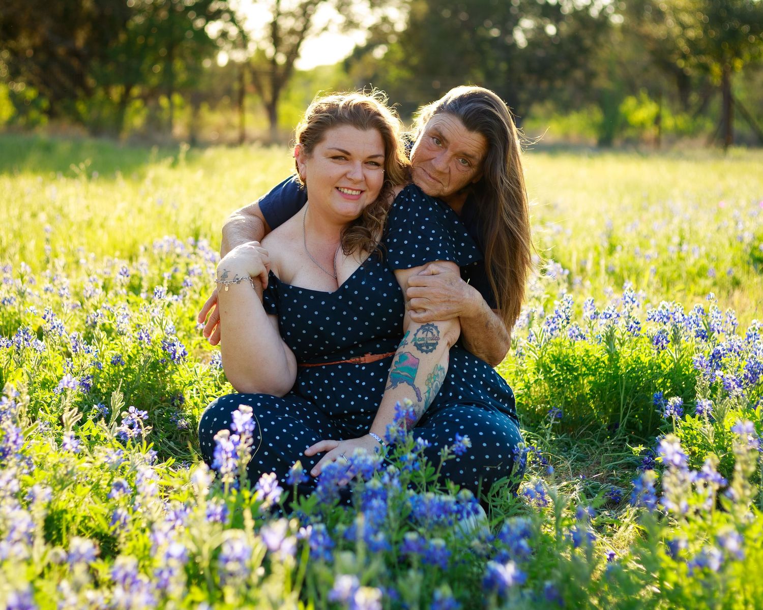 Couple sitting together in a field of blooming bluebonnets, smiling warmly in matching navy polka dot outfits.