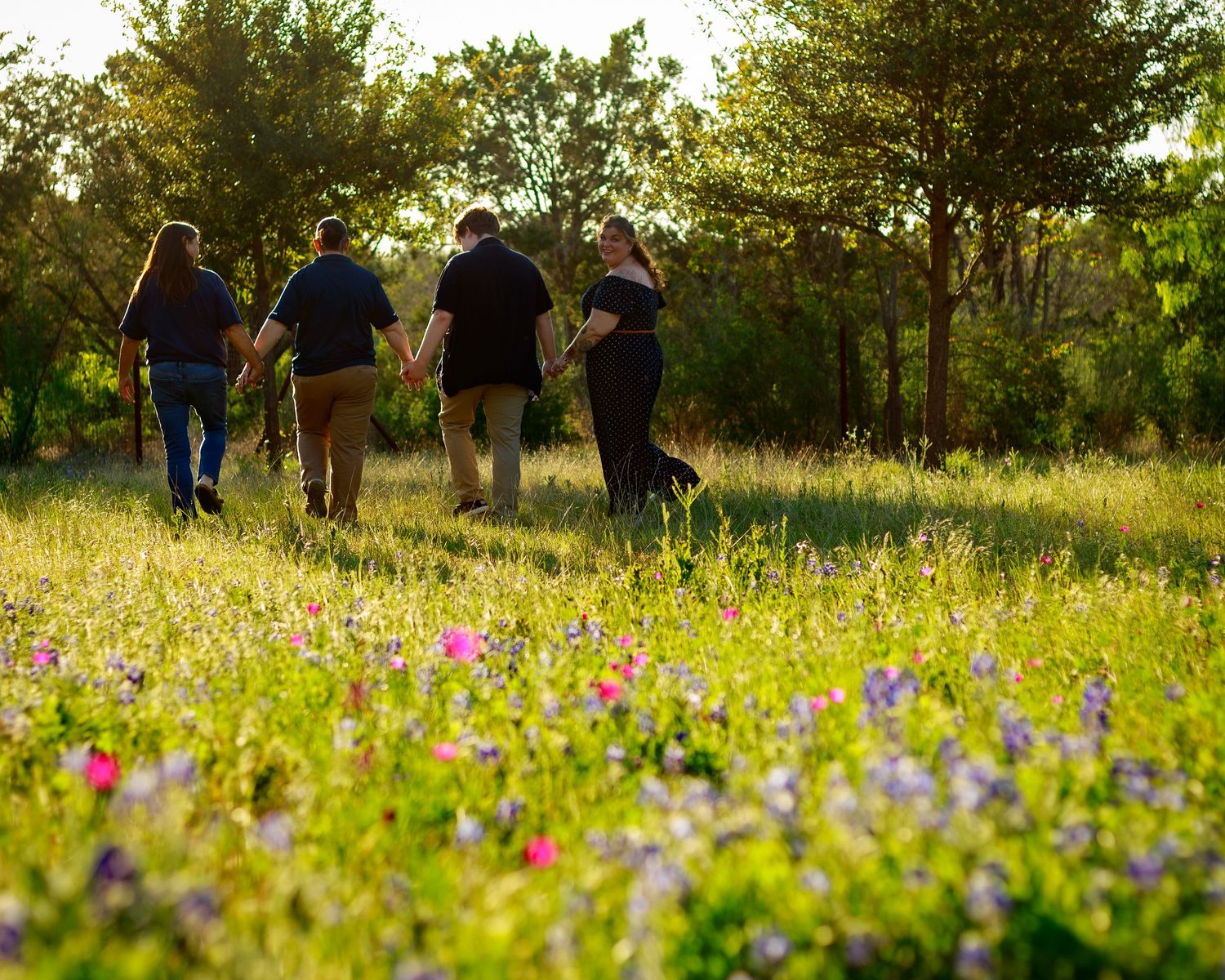 Family walking hand-in-hand through a sunlit wildflower meadow with pink and purple blooms at golden hour.