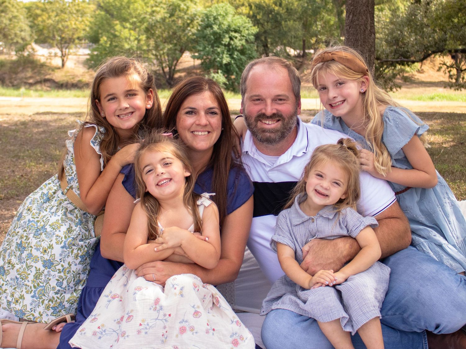Happy family group poses together outdoors in coordinated blue and white outfits.