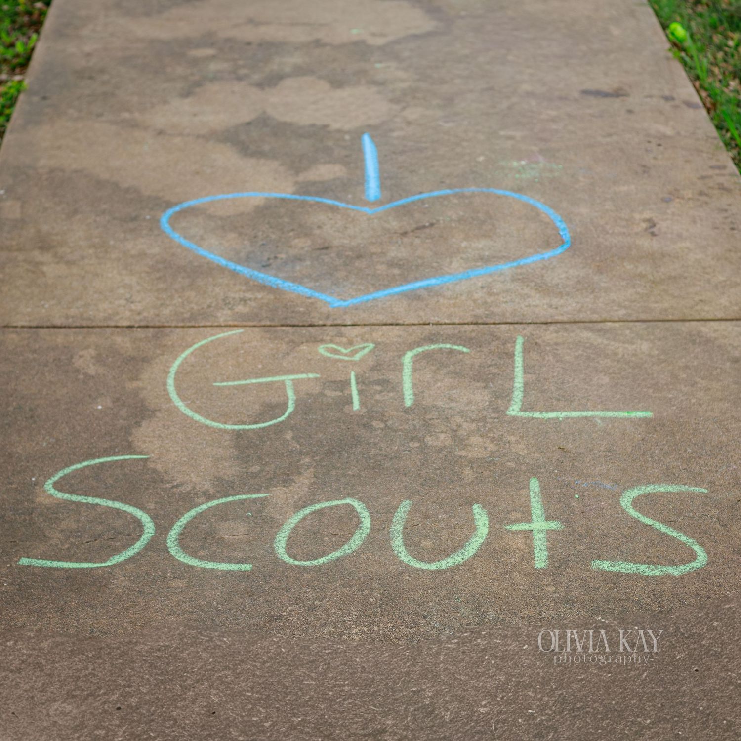 Chalk drawing on sidewalk with blue heart and green text reading Girl Scouts.