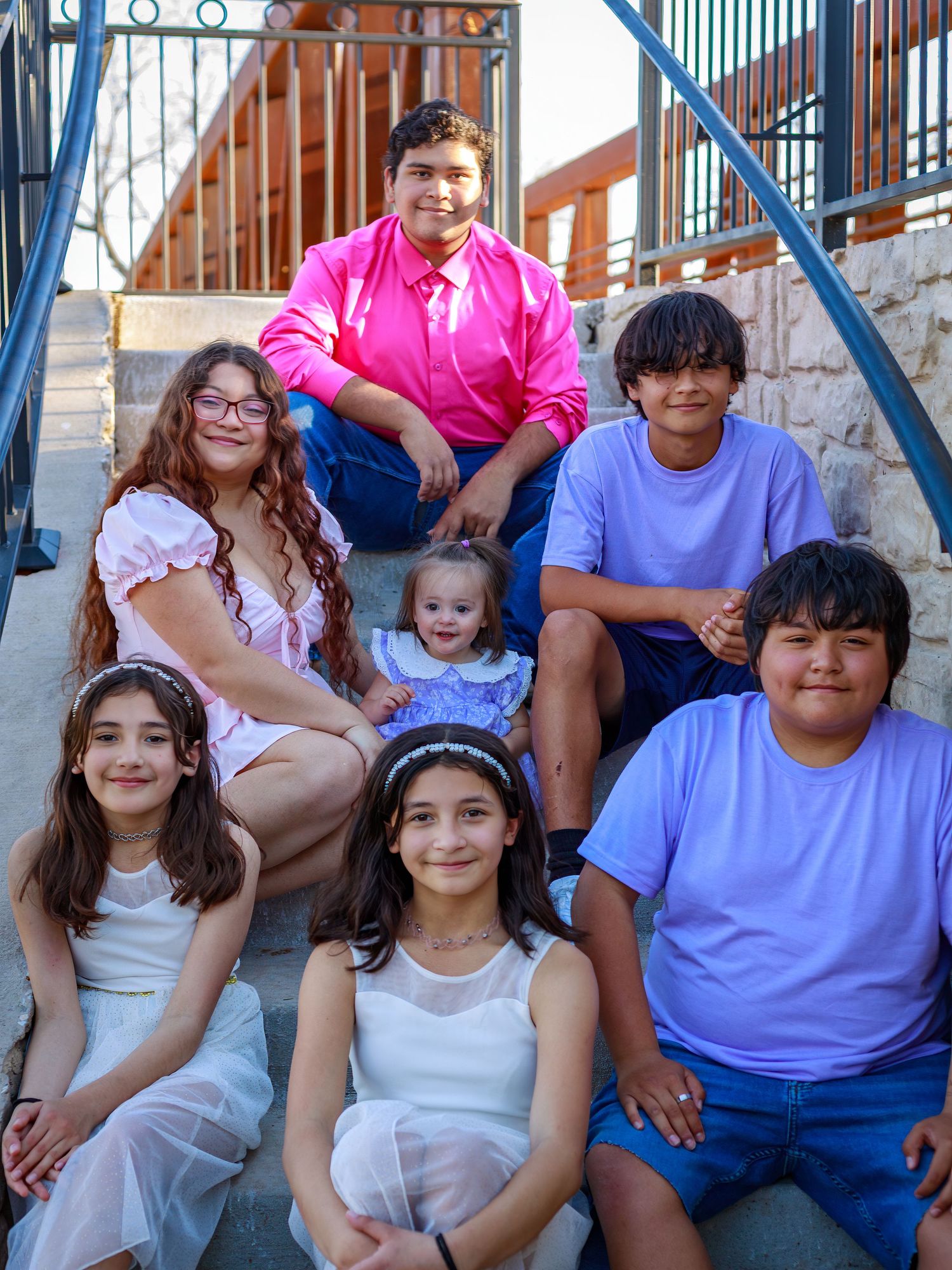 Group of seven children posing together on outdoor steps, dressed in colorful outfits, smiling for a family photo.